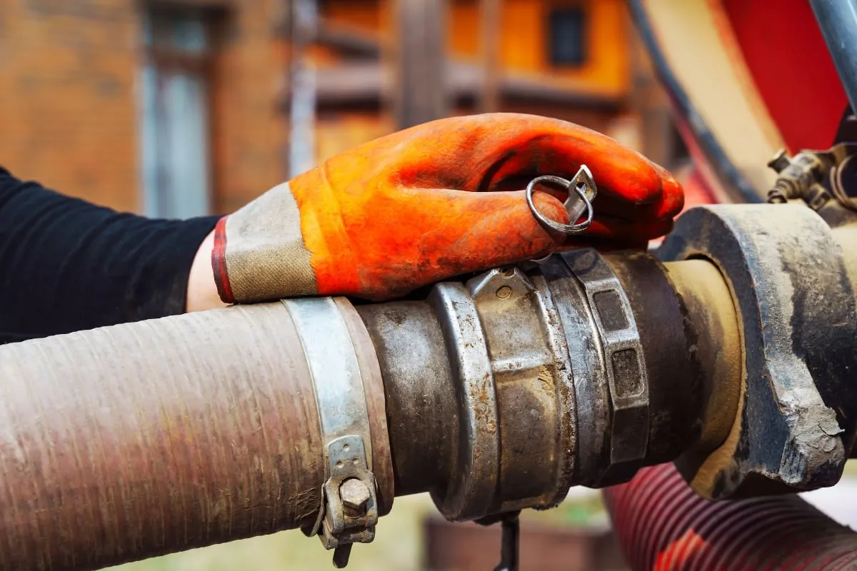 A hand wearing a gloves while fixing a plumbing tube