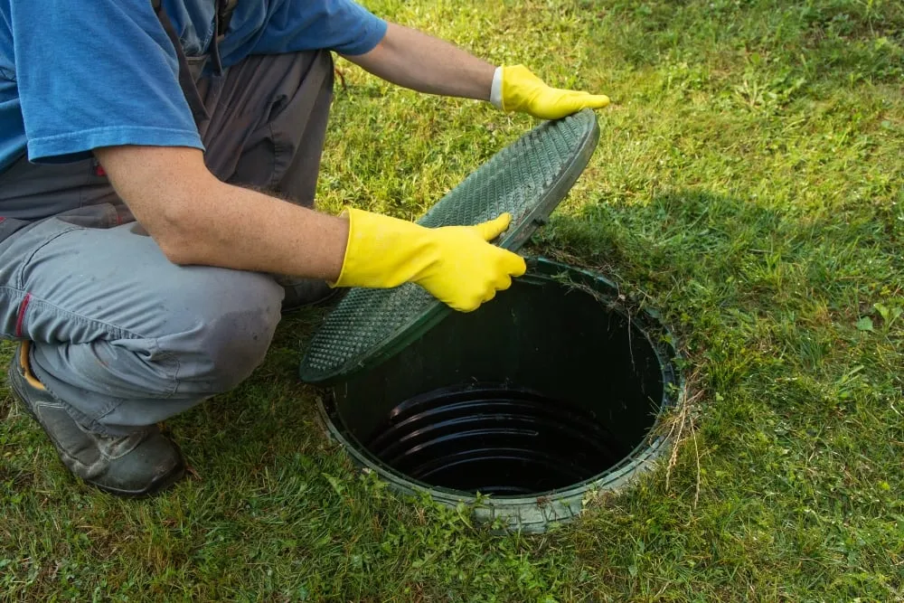 a person wearing a yellow gloves and opening the septic tank cover