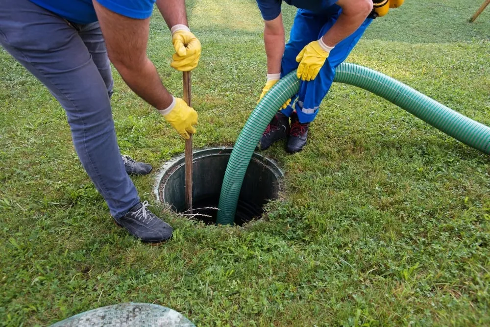 Two workers running a suction hose into a septic tank during a pump-out
